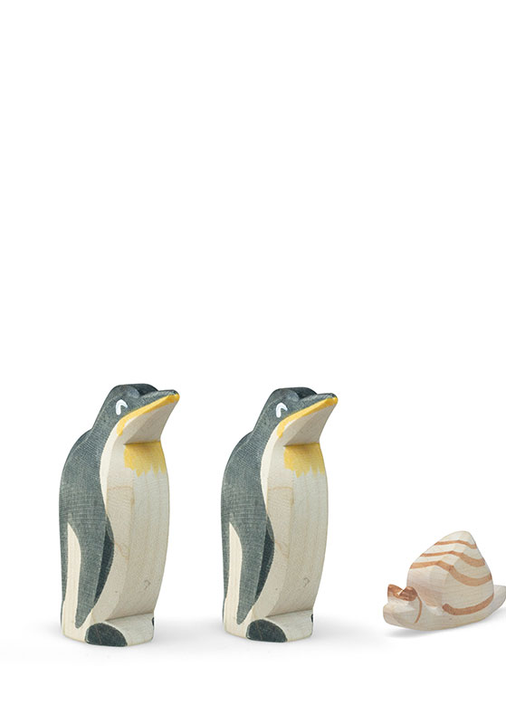 Two carved wooden penguin figurines standing side by side with a small striped seashell on a white background.