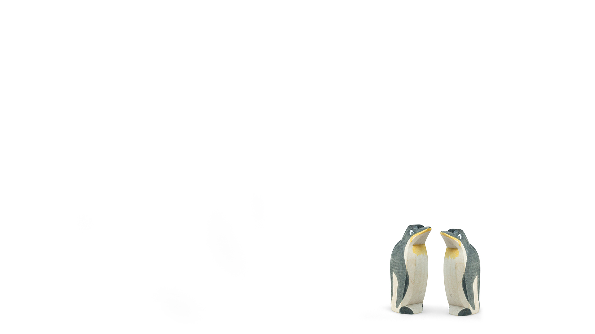paarberatung Two wooden penguin figurines with cream bodies, dark blue-gray wings, and yellow beaks standing together on a white background.
